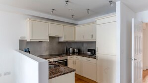 A compact kitchen with white cabinets, a granite countertop, a built-in oven, a microwave, and a coffee maker.