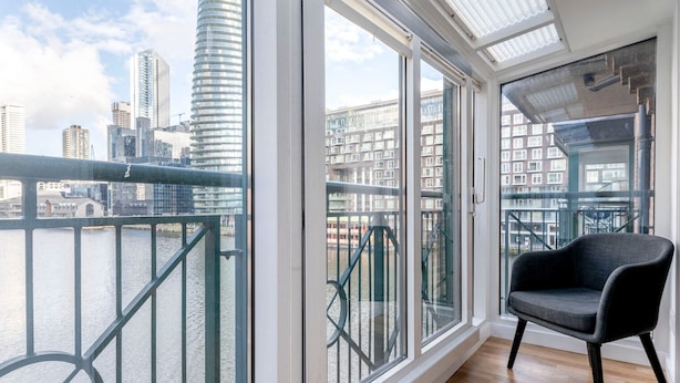 A balcony with a view of a cityscape, a chair, and a glass railing.