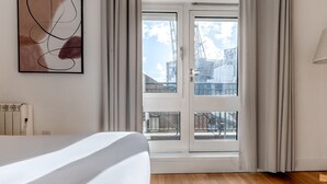 A hotel room with a large bed, a view of the city through a glass door, and a radiator on the wall.