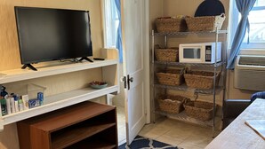 Une pièce avec un téléviseur posé sur une étagère, un four à micro-ondes sur un meuble et des paniers sur des étagères.