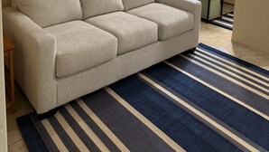 Une pièce avec un canapé beige, un tapis à rayures, un lit superposé et des rideaux aux fenêtres.