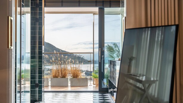 A modern interior with a glass door leading to a balcony with a view of a body of water and hills. - Busan Nunuhouse Poolvilla Pension (Busan)