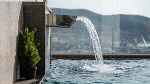 A water feature with a waterfall, a potted plant, and a view of a cityscape through a window. - Busan Nunuhouse Poolvilla Pension (Busan)