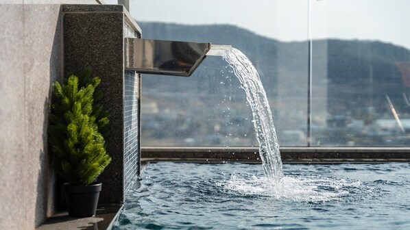 A water feature with a waterfall, a potted plant, and a view of a cityscape through a window.