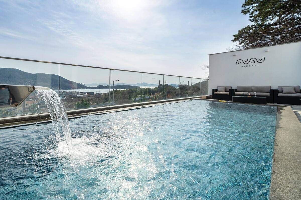 A rooftop infinity pool with a waterfall feature, overlooking a scenic view of mountains and a body of water.