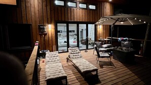 A wooden deck with lounge chairs, a TV, and a covered area with tables and chairs. - Modern Savary Island Cottage – Perfect Family Getaway & Kids’ Favorite! (Savary)