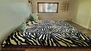 A room with a zebra-patterned bedspread, a window with a view of trees, and a wooden ladder leaning against the wall. - Modern Savary Island Cottage – Perfect Family Getaway & Kids’ Favorite! (Savary)