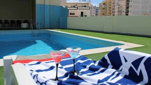 A pool area with a lounge chair and two martini glasses on a blue and white towel. - Apartamento Mar Azul (Portimão)