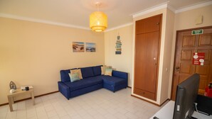 A living room with a blue sofa, a small table, a television, and a wooden door. - Apartamento Mar Azul (Portimão)