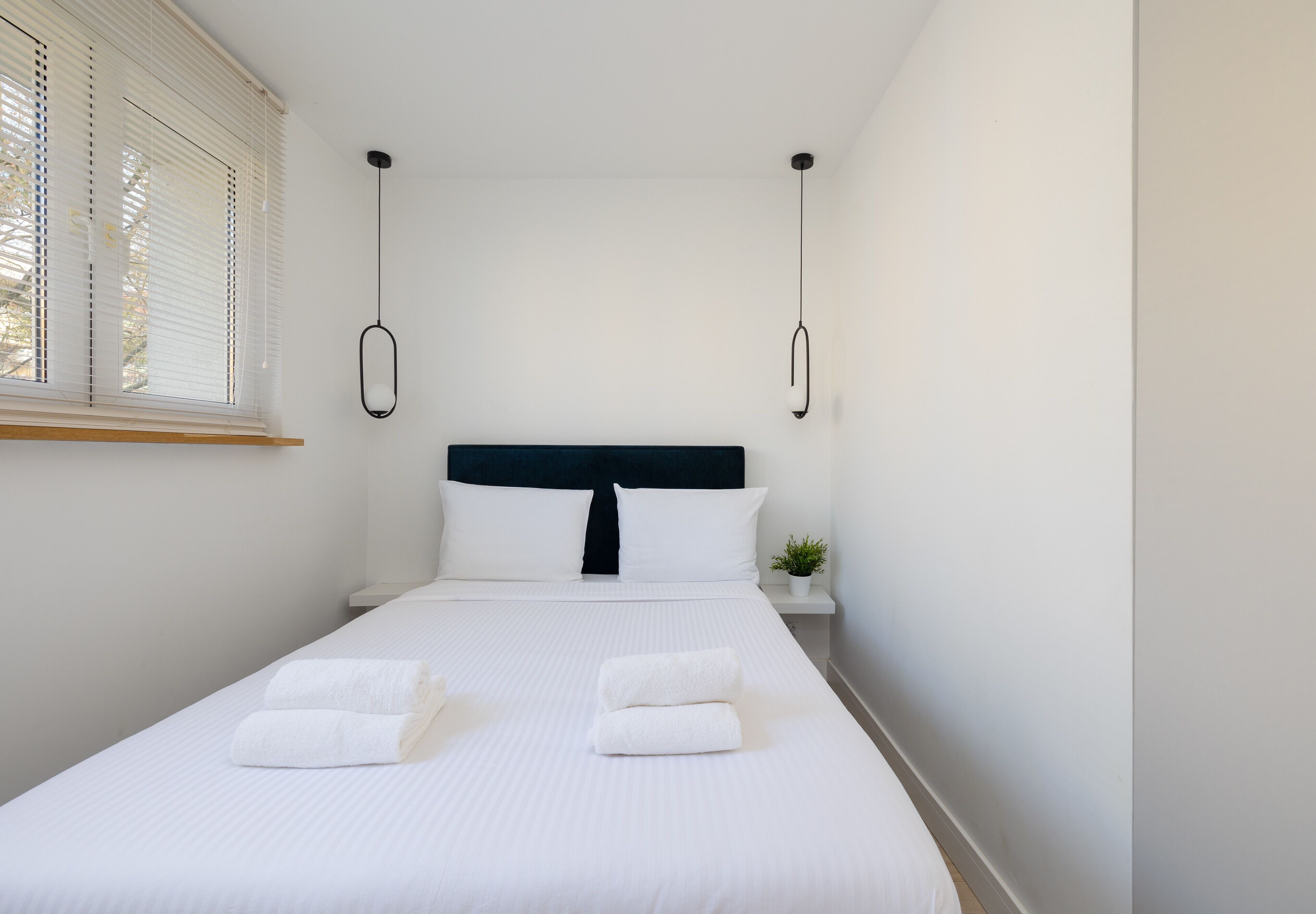 Een net opgemaakt bed met witte lakens en twee opgevouwen handdoeken, een zwart hoofdeinde en een kleine kamerplant.