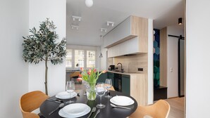 Un coin repas moderne avec une table ronde dressée pour quatre personnes, entourée de chaises en bois. Une plante en pot et un vase rempli de fleurs sont posés sur la table.