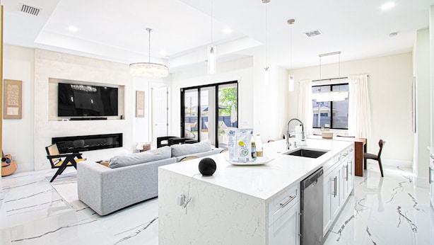 A modern kitchen with a central island, a dining area with a table and chairs, and a living room with a sofa and a television.