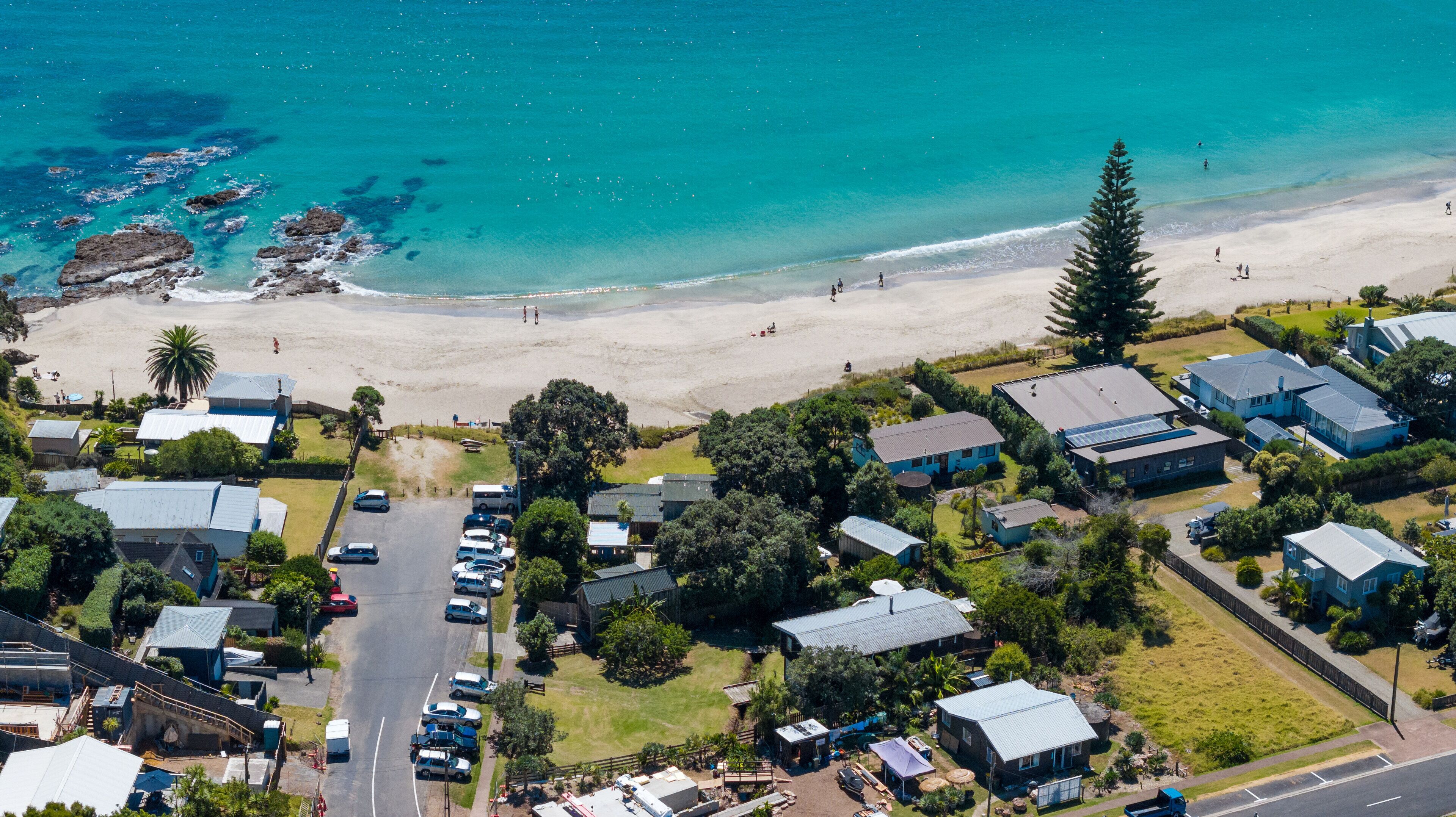 An aerial view of a coastal residential area with houses, a beach, and clear blue waters.