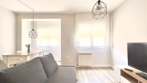 Un salon moderne avec un canapé gris, une table basse en bois, un téléviseur posé sur un meuble en bois et deux lampes suspendues.