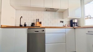 Une cuisine compacte avec des meubles blancs, un lave-vaisselle en acier inoxydable et un plan de travail en bois.