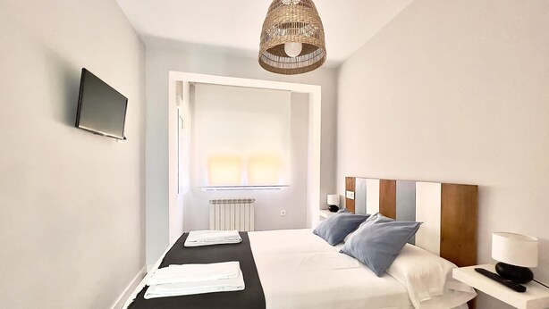 Une chambre à coucher moderne avec un lit, des tables de chevet, un téléviseur et une fenêtre.