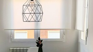 Un coin repas comprenant une table, des chaises, un luminaire suspendu et une fenêtre avec des stores.
