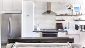 Una cocina moderna con armarios blancos, un refrigerador de acero inoxidable, una estufa a gas y un horno empotrado.