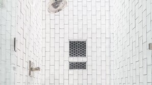 Una ducha con puerta de vidrio, cabezal de ducha y pared de azulejos con un diseño geométrico.