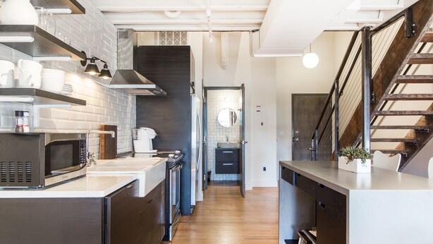 A modern kitchen with a stainless steel microwave, a coffee maker, and a sink. There is a wooden staircase leading to another level. - Spacious Loft, 2 Blocks from Broadway! (Loft 302) (Nashville)