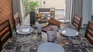 A dining table set with plates, cups, a bread basket, and a pitcher, surrounded by chairs.
