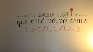 A neatly made bed with white linens and rolled towels, a wall with a motivational quote in Portuguese, and a simple, clean room design.