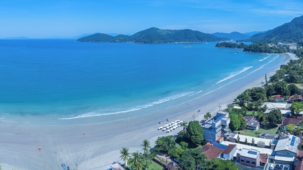 A beach with clear blue waters, a sandy shore, and surrounding hills.