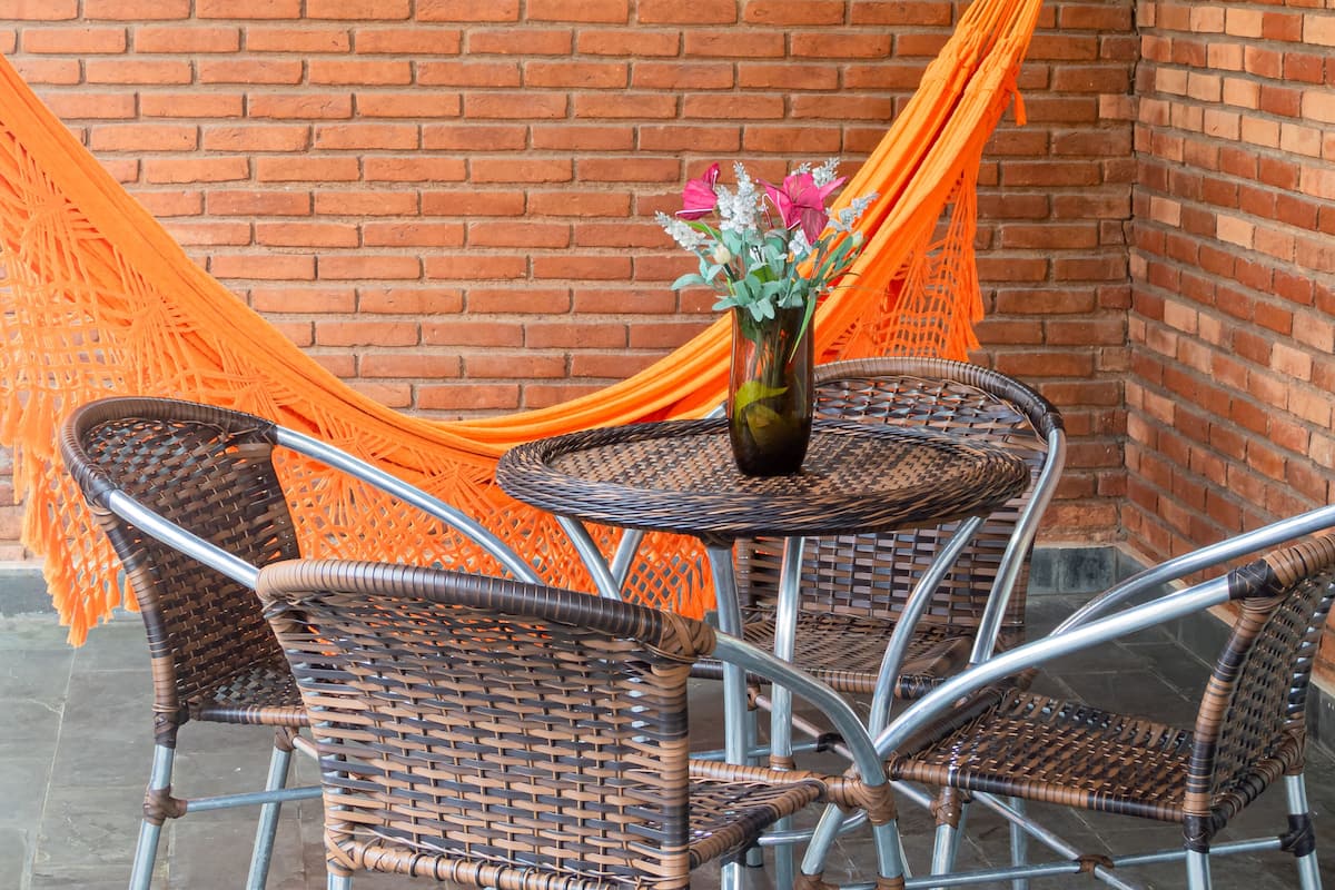 A wicker table and chairs set against a brick wall, with an orange hammock draped over the chairs.