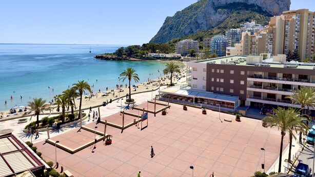 A coastal area with a beach, a large rock formation, and residential buildings. - 16sapphire first line (Calp)