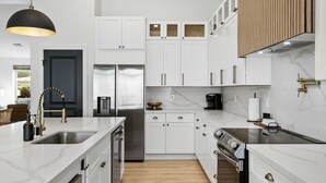 Una cocina moderna con armarios blancos, un refrigerador de acero inoxidable, horno empotrado y encimera de mármol.