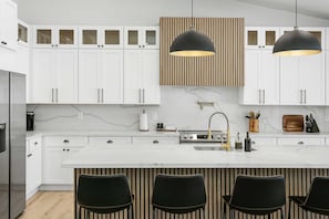 A modern kitchen with white cabinets, a marble countertop, two pendant lights, and a central island with bar seating.
