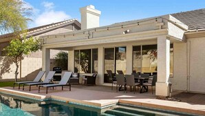 Un espacio al aire libre cubierto con piscina, sillones de descanso y una mesa de comedor.