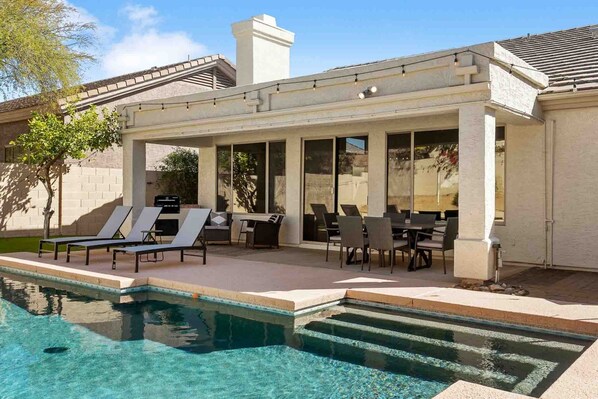 A covered outdoor area with a pool, lounge chairs, and a dining table. - SWSS Upscale Kierland 4BR Retreat | Heated Pool, Outdoor Living, Gourmet Kitchen & Fire Pit (Scottsdale)