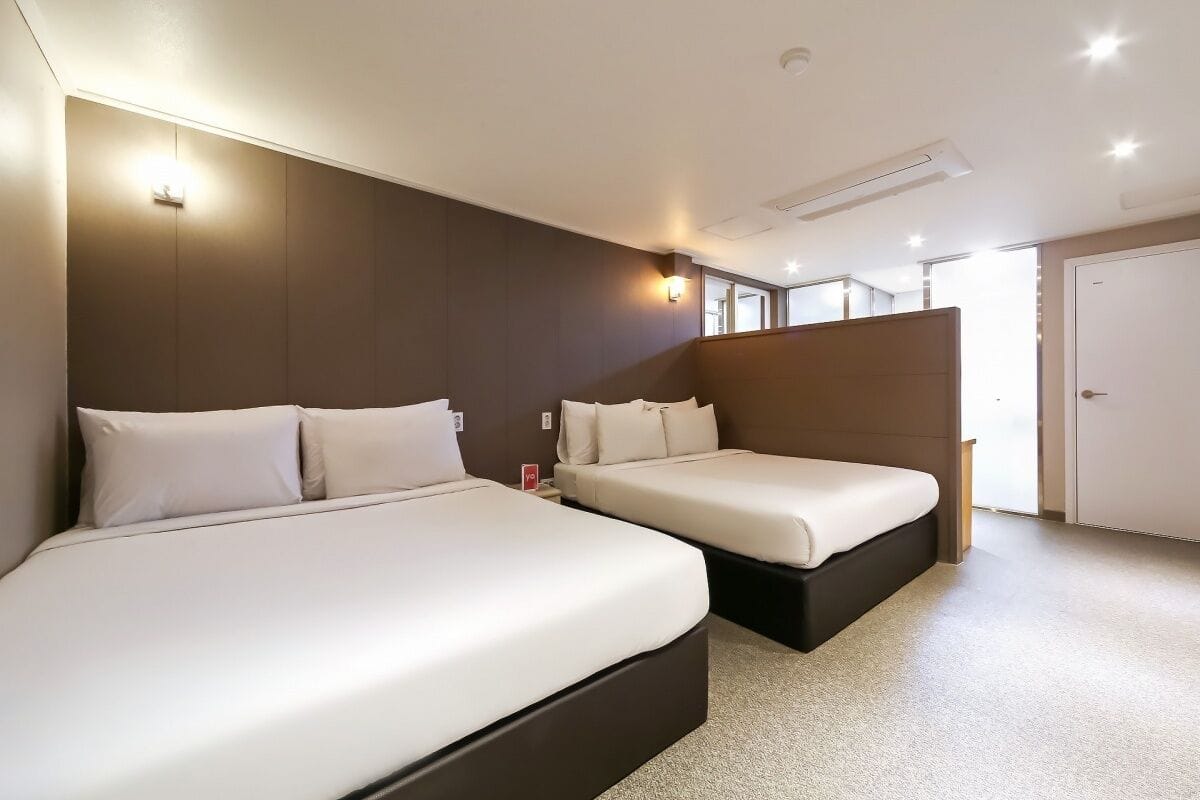 A hotel room with two beds, a large window, and a door.
