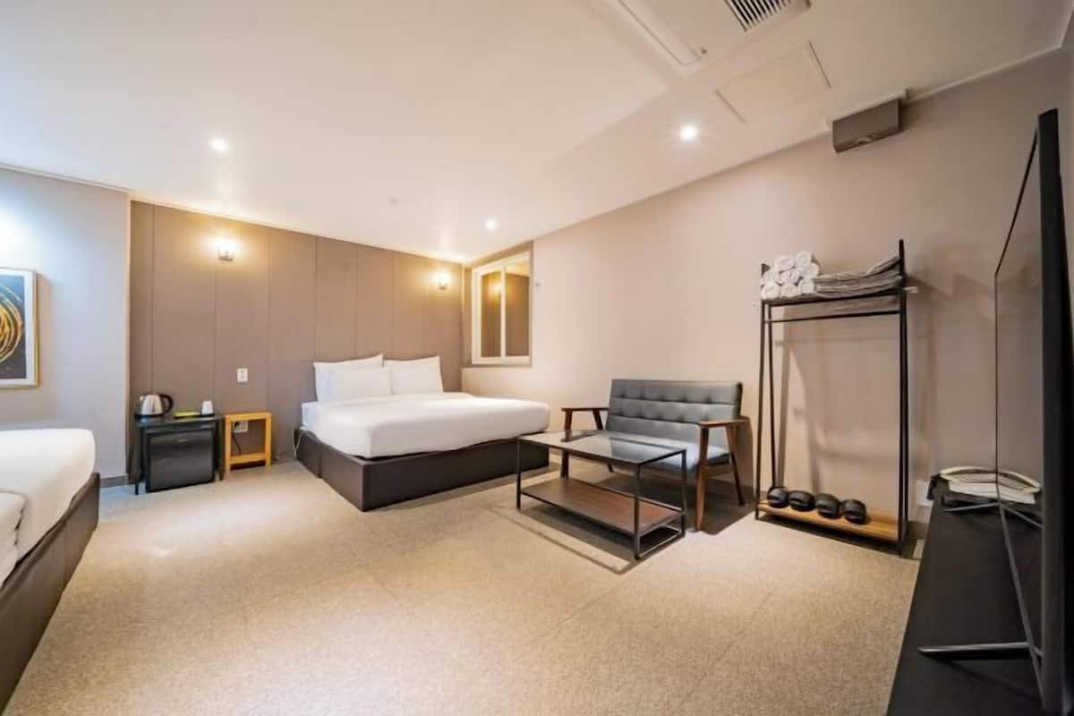 A modern hotel room with a bed, a seating area, a TV, and a shoe rack.