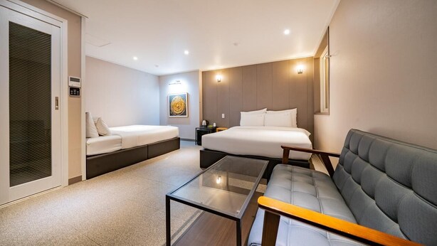 A modern hotel room with a bed, two sofas, a glass coffee table, and a small side table. - ymotel (Busan)