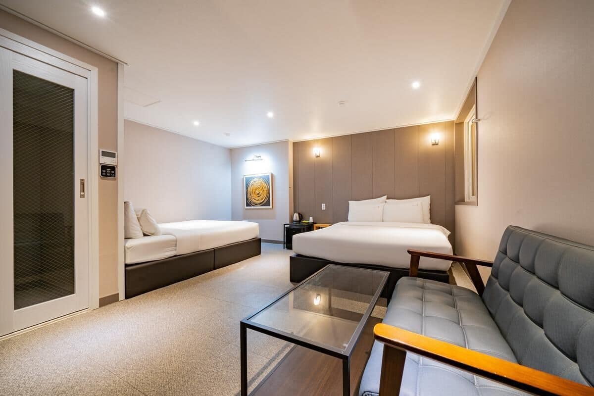 A modern hotel room with a bed, two sofas, a glass coffee table, and a small side table.