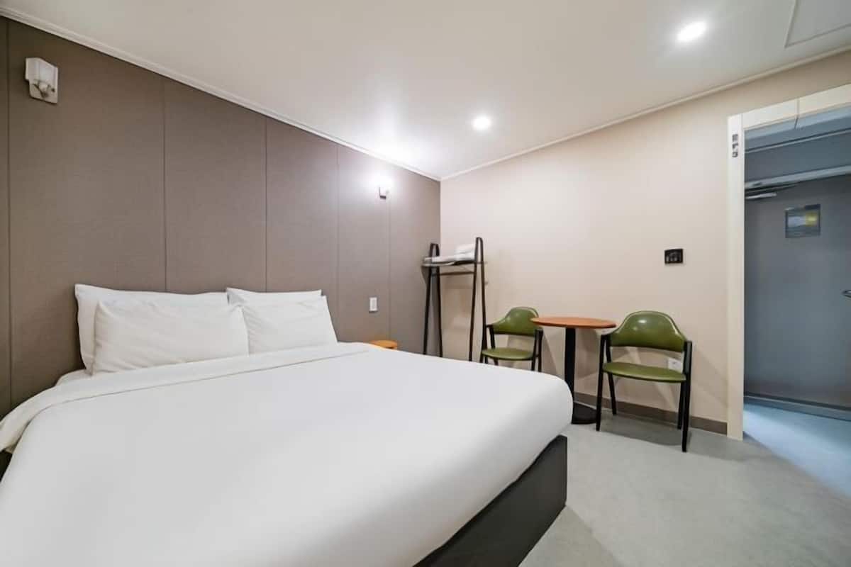 A hotel room with a bed, a desk, two chairs, and a door.