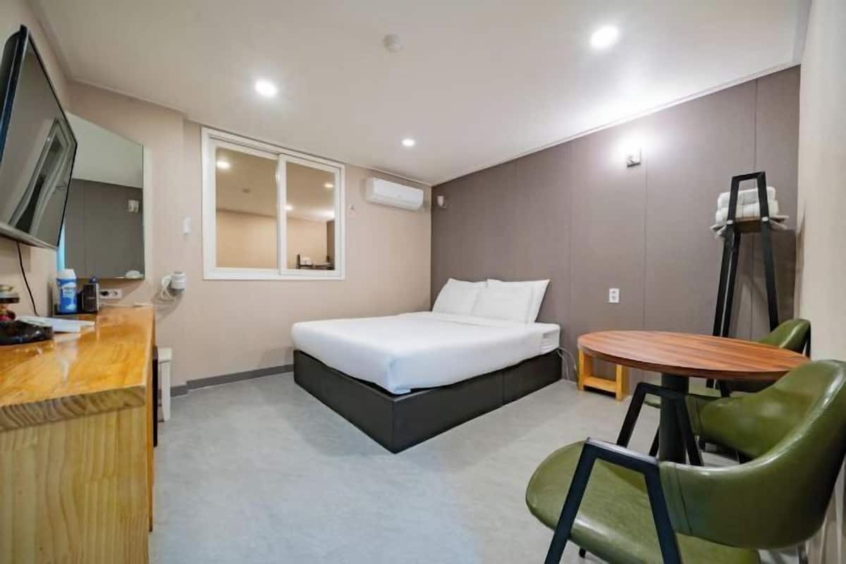 A hotel room with a bed, a desk, a chair, a TV, and a window.