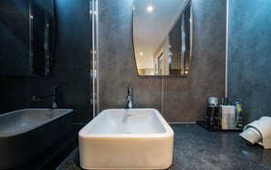 Un baño moderno con un lavamanos rectangular, un espejo grande y una pared de tonos oscuros.