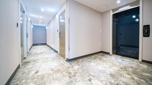 A hallway with a marble floor, a door on the left, and an elevator on the right. - ymotel (Busan)