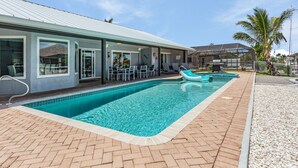 A swimming pool area with a tiled deck, lounge chairs, and a covered seating area. - Gulf Access, Beautiful Water Views, Paddle Board, Heated Pool - Villa Manhattan - Roelens (Cape Coral)