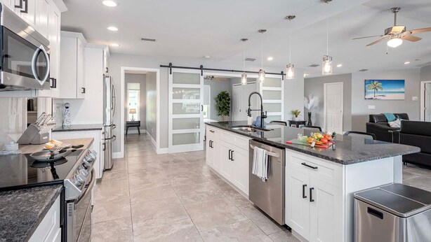 A modern kitchen with white cabinets, stainless steel appliances, and a central island with a sink. - Gulf Access, Beautiful Water Views, Paddle Board, Heated Pool - Villa Manhattan - Roelens (Cape Coral)