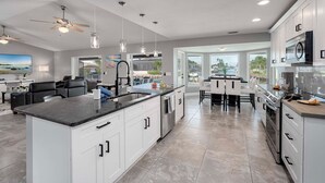 A modern kitchen with white cabinets, a large island, and a dining area with a view. - Gulf Access, Beautiful Water Views, Paddle Board, Heated Pool - Villa Manhattan - Roelens (Cape Coral)