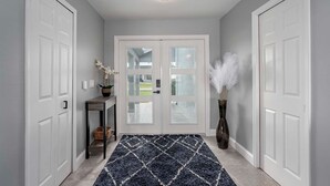 A hallway with a patterned rug, a potted plant, and a vase with white feathers. - Gulf Access, Beautiful Water Views, Paddle Board, Heated Pool - Villa Manhattan - Roelens (Cape Coral)