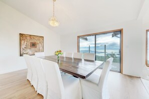 Enjoy meals in this dining room with a large table, white chairs, and a chandelier, offering a view of the surrounding mountains.