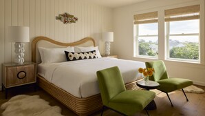 A bedroom with a large bed, two nightstands, two green chairs, a small table with flowers, and a view of greenery through the window. - NEW Wellness Focused Adult Only Boutique Hotel - Standard Suite ADA Compliant (Rodanthe)