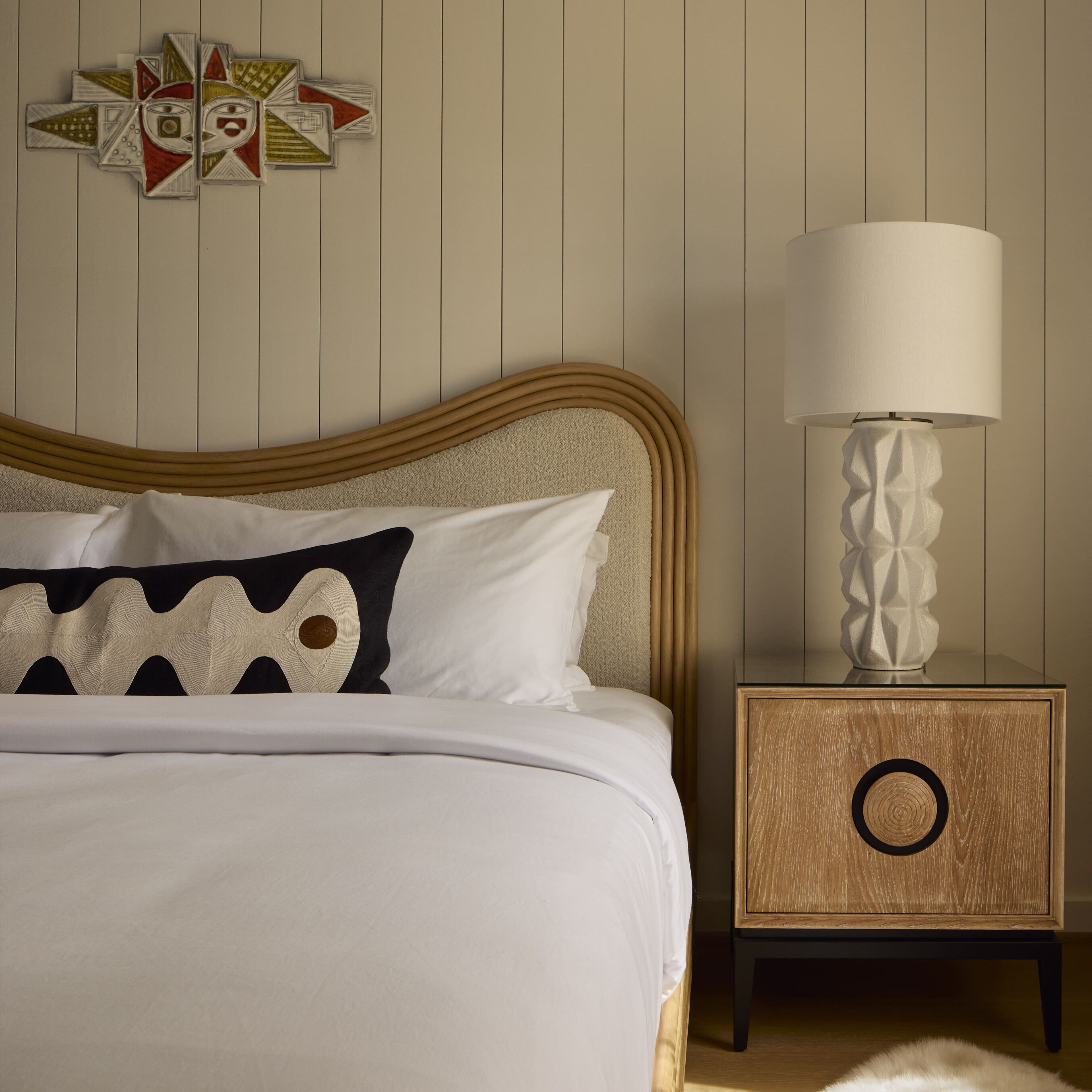 A neatly made bed with white and black bedding, a wooden headboard, and a bedside table with a lamp.
