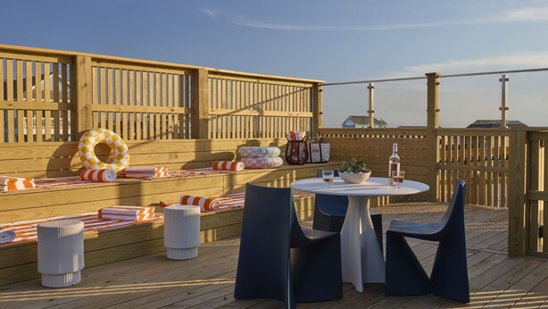Eine Holzterrasse mit rundem Tisch und Stühlen, einer Bank mit Kissen sowie einem Rettungsring.