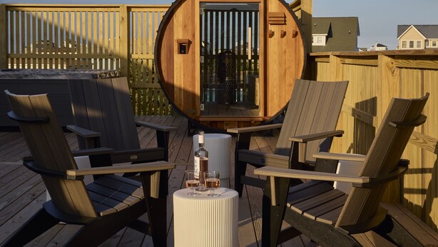 Une terrasse en bois avec une structure circulaire également en bois, qui pourrait être un sauna ou un jacuzzi, et deux chaises longues.